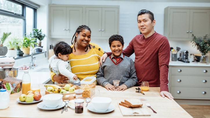 A family standing in the kitchen with a healthy meal on the table.