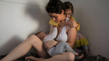 Mother breastfeeding her infant and comforting her older child during an emergency.