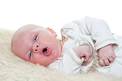 Infant lying down on blanket, coughing.